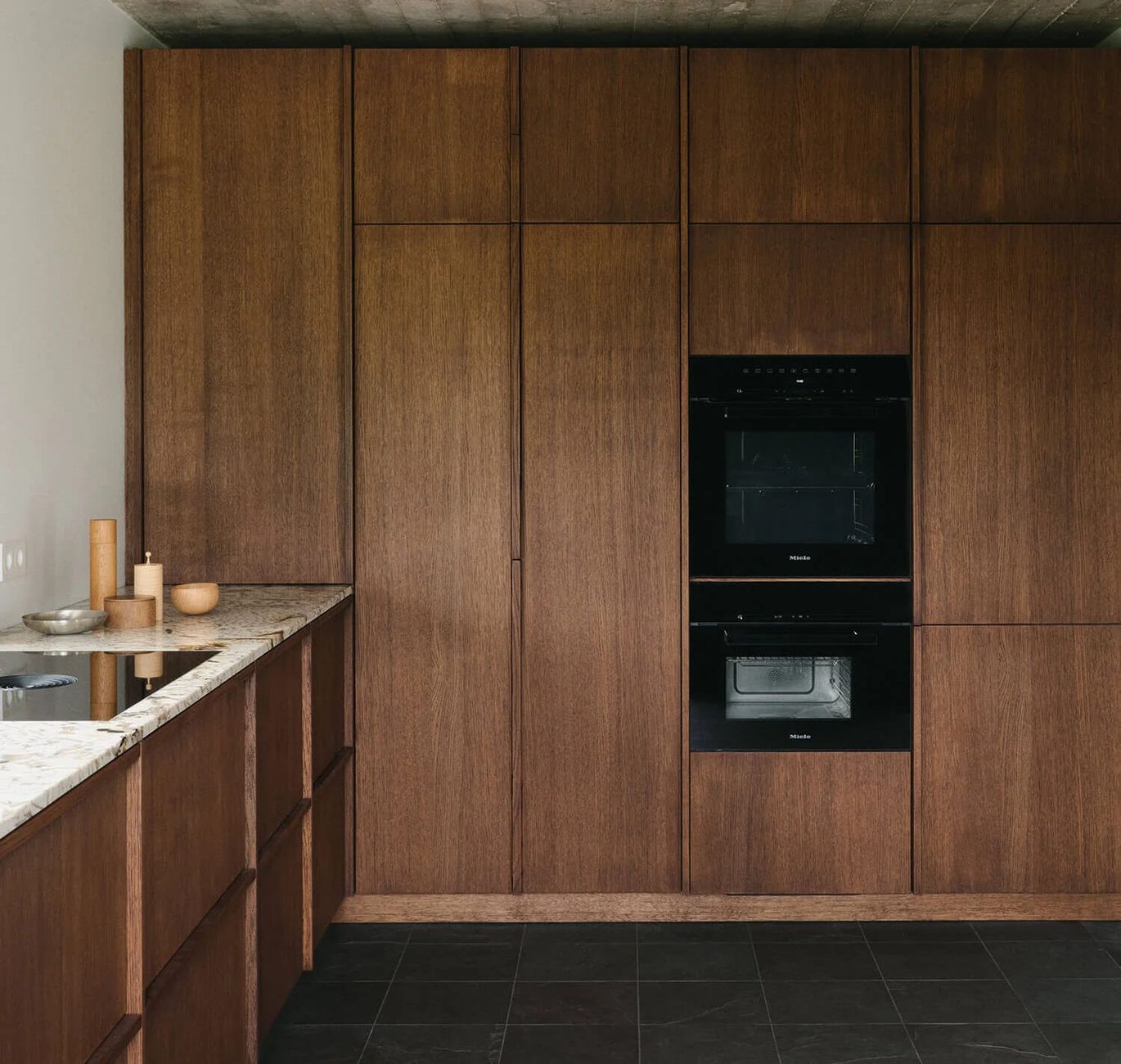 Eine moderne Küche mit eleganten, dunklen Holzschränken und eingebauten schwarzen Backöfen. Die Arbeitsplatte besteht aus Granit