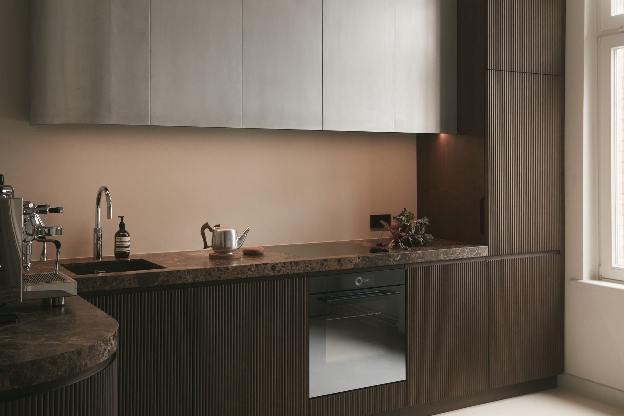 Eine elegante, moderne Küche mit dunklen Holzschränken, Marmorarbeitsplatten, einem Einbaubackofen und einer Spüle aus Edelstahl